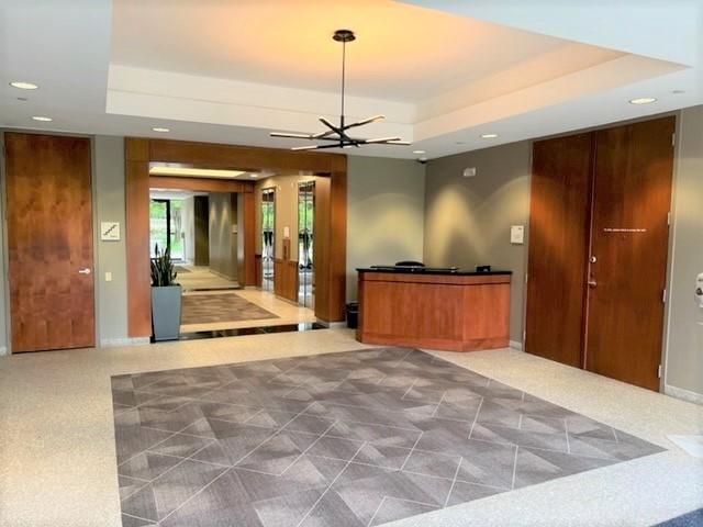 cherry wood doors and reception desk open the white and grey lobby. Yellow light comes from the abstract chandelier. 